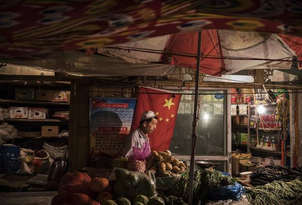 An ethnic Uyghur shopkeeper works next to a Chinese flag at his shop on June 29, 2017 in the old town of Kashgar, in the far western Xinjiang province, China.