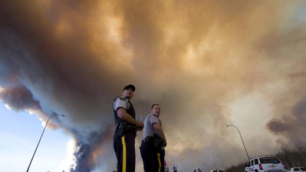Police officers direct traffic under a cloud of smoke from a wildfire in Fort McMurray, Alta., on May 6, 2016.